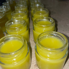 Body balm in small glass jars, yellow balm, clear glass, lined up on surface
