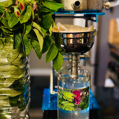 Rose Hydrosol bottle with clear glass and blue label, stainless steel filter, and green leaves