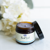 Facial cleanser jar with brown glass, black lid, and blue scrub inside, Herbesque label visible