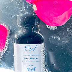 Face serum bottle with black glass, white label, and pink rose petal in water