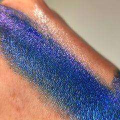 Eyeshadow swatch with blue and purple shimmer on skin, showing texture and color gradient