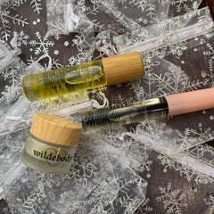 Body oil bottles with wooden caps, clear tubes, and "wildebody" text on a jar, on a snowflake background