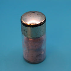 Spice jar with metal lid, clear glass, and pink contents on blue background