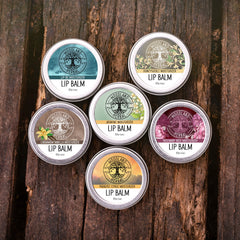Lip balm tins with Woodland Herbal logo, various colors and floral designs, on wood surface