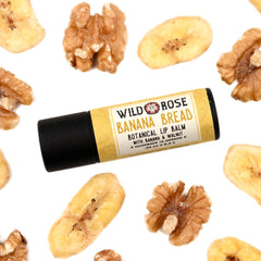 Lip balm tube with black cap and yellow label, Wild Rose brand, surrounded by walnuts and banana slices