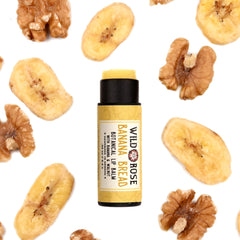 Lip balm tube with yellow label, black cap, and "Wild Rose Banana Bread" text, surrounded by banana slices and walnuts