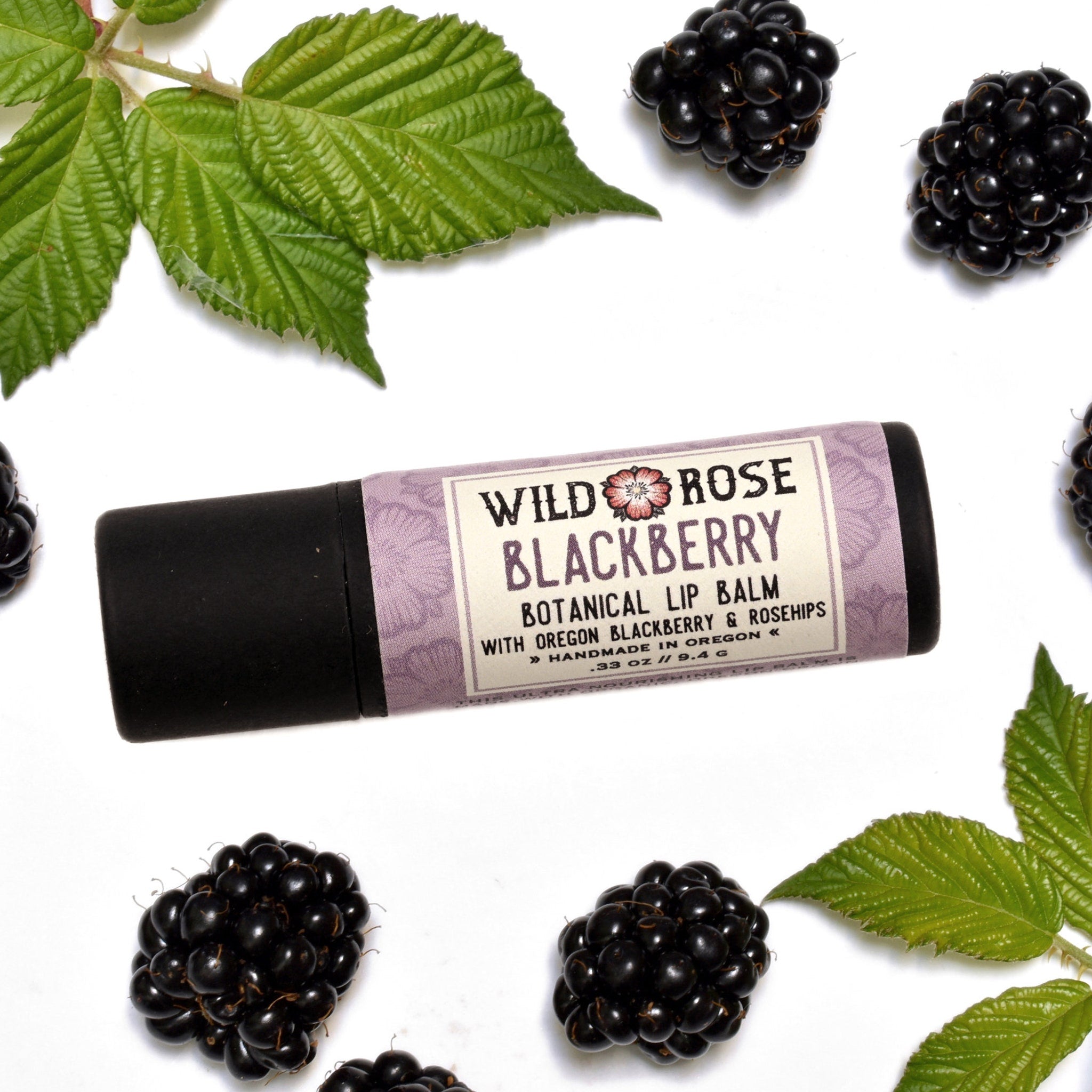Lip balm with black tube and Wild Rose label, blackberries and green leaves on white background