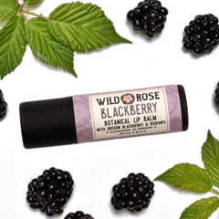 Lip balm with black tube and Wild Rose label, blackberries and green leaves on white background