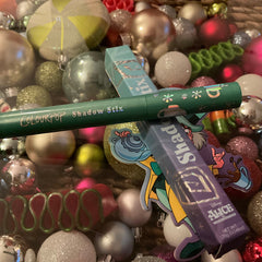 Colourpop Shadow Stix green and purple tubes with text, surrounded by Christmas ornaments