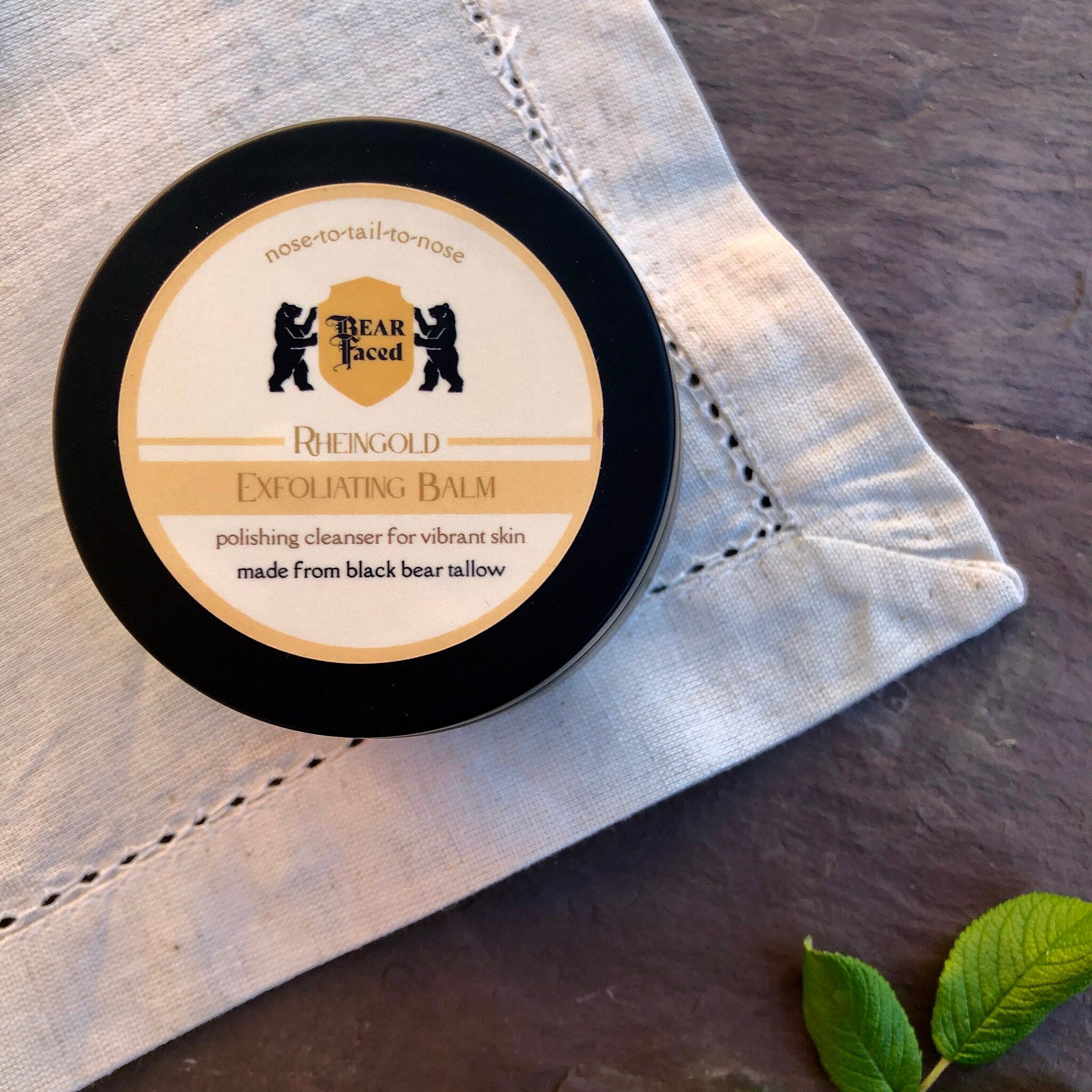 Skin care exfoliating balm, black round container, white label with text, on white cloth