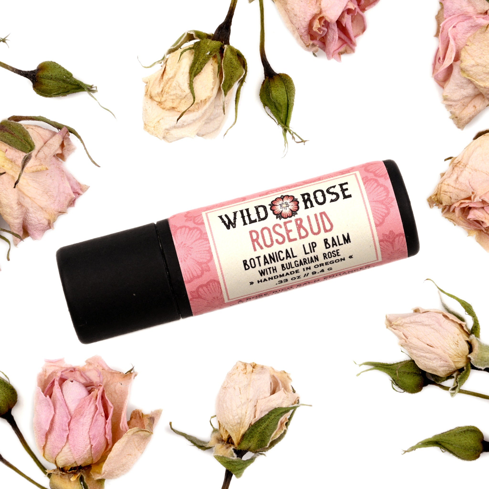 Lip balm with pink floral pattern, black tube, and ROSEBUD brand name, surrounded by dried roses