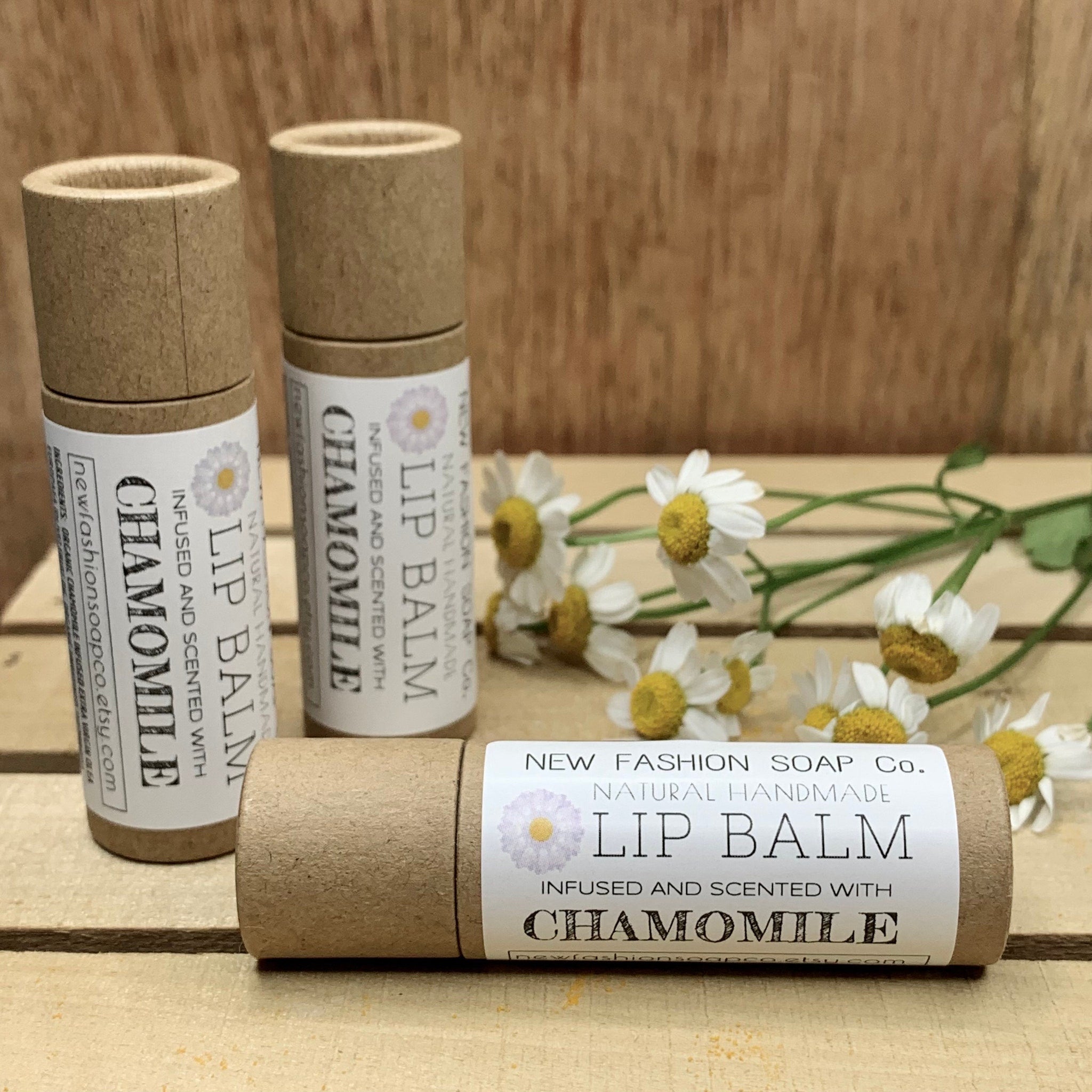 Lip balm tubes in brown cardboard with white label, NEW FASHION SOAP Co. branding, and chamomile flowers