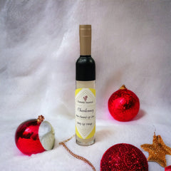 Lip gloss bottle with black and gold cap, yellow label, and red Christmas ornaments on white fabric