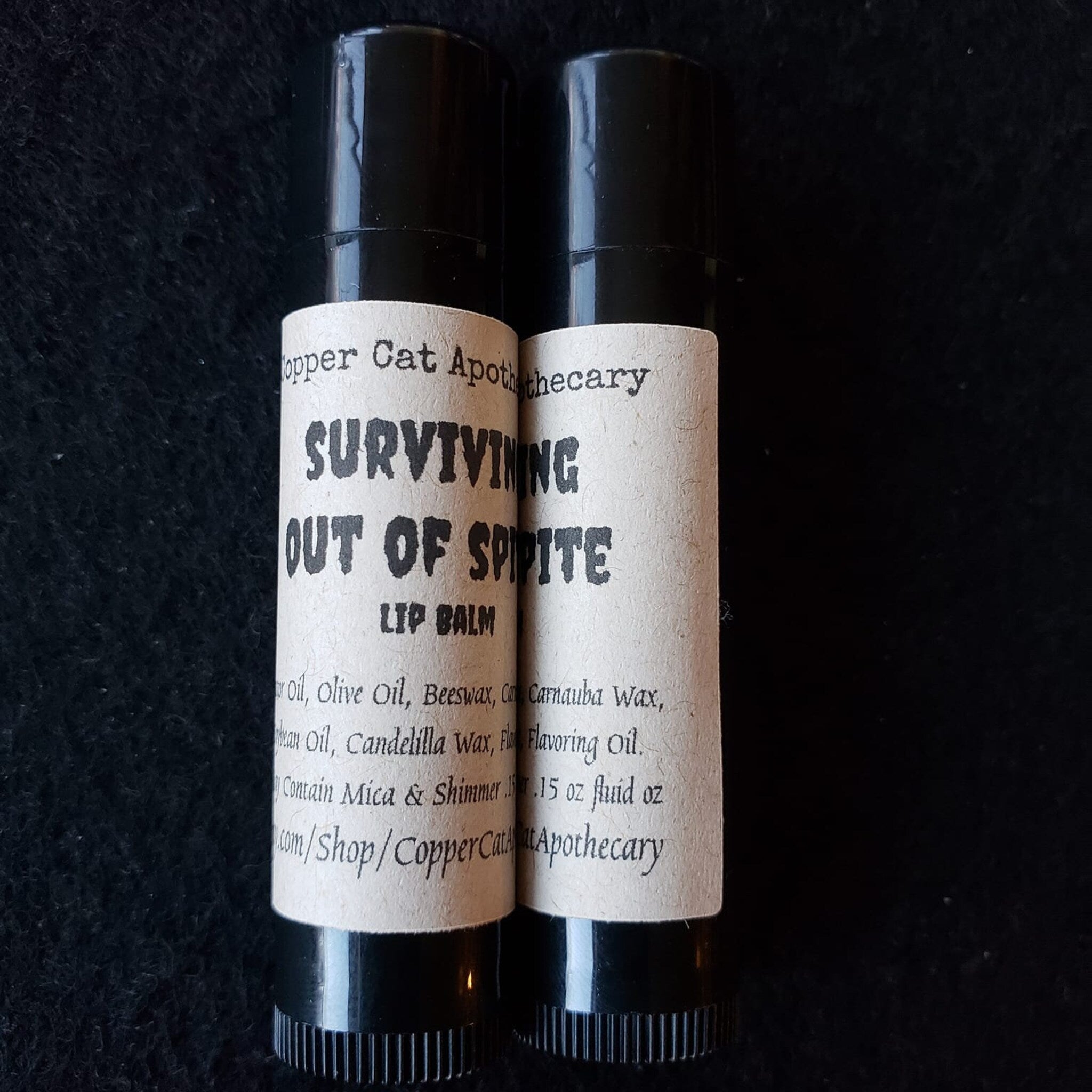 Lip balm tubes with black caps and paper labels, "Surviving Out Of Spite" brand name visible