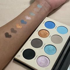 Eyeshadow palette with blue, gold, and gray shades, heart-shaped swatches on arm, palette visible