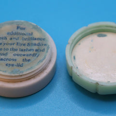 Eye shadow container, off-white and green plastic, open lid, blue text on top, on blue surface