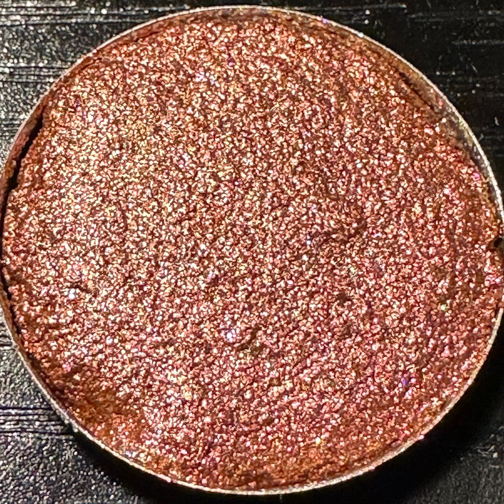 Pressed eyeshadow pan with rose gold duochrome glitter in a 26mm round compact