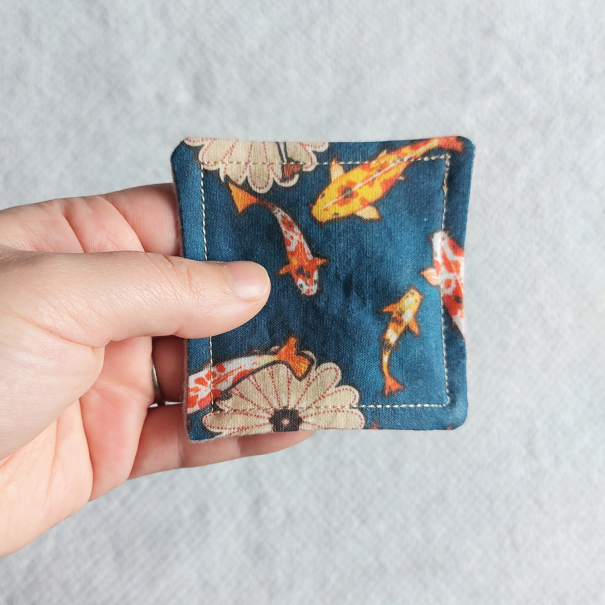 Makeup remover pad, blue fabric with fish pattern, held in hand