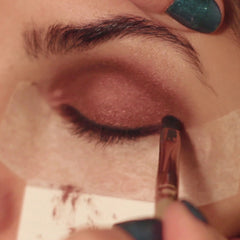 Eyeshadow application with brown eyeshadow, brush, and green nail polish on fingers