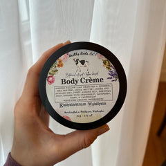 Hand scooping whipped tallow cream from a glass jar, showing rich texture and botanical infusion