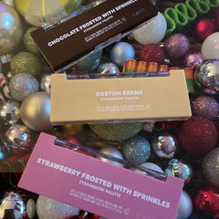 Eyeshadow palette in brown, pink, and tan with white text, on a surface of ornaments.