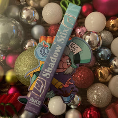 Eyeshadow stick, blue and purple packaging, "Shadow Stix" text, Alice in Wonderland design