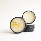 Lip balm tins, black metal containers with yellow petals, open to show balm inside