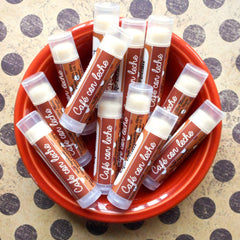 Lip balm tubes in a red bowl, brown and white Cafe con Leche label, clear cap, beige balm inside