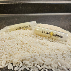 Lip balm tubes with yellow balm, clear plastic, and "BALM SQUAD" text, on white rice