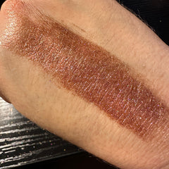 Close-up of pressed glitter eyeshadow pan showing rose gold duochrome shimmer and fine sparkle texture