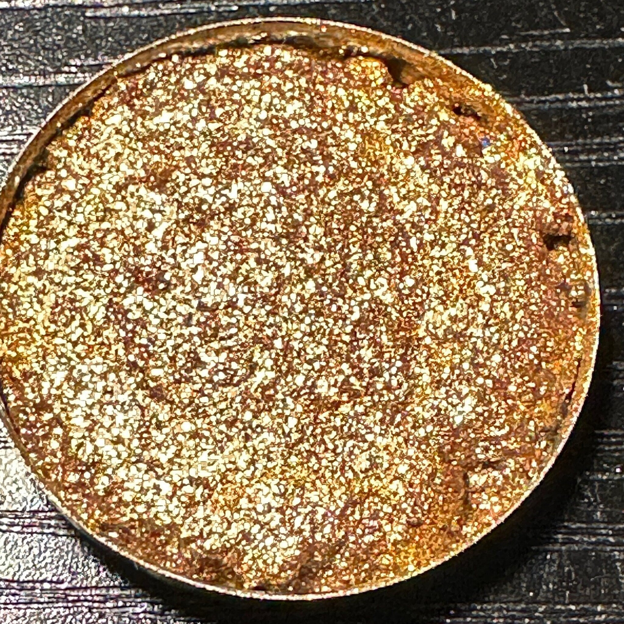 Single pressed eyeshadow pan with light gold and champagne duochrome glitter finish, circular shape in black compact.