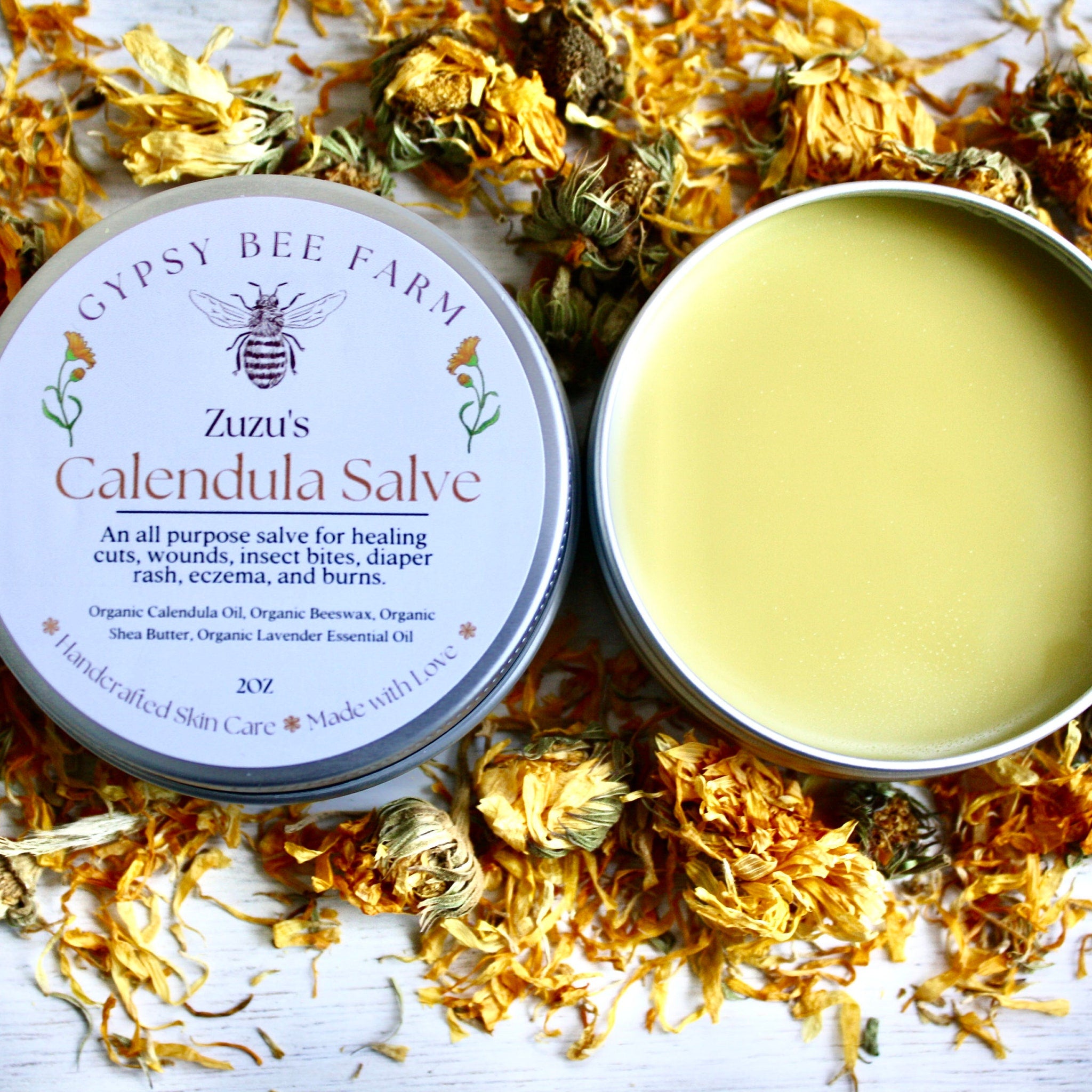 Calendula Salve, yellow salve in metal tin, surrounded by dried orange flower petals, Zuzu's brand visible