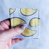 Makeup remover pad, paisley fabric, yellow and blue pattern, held by hand