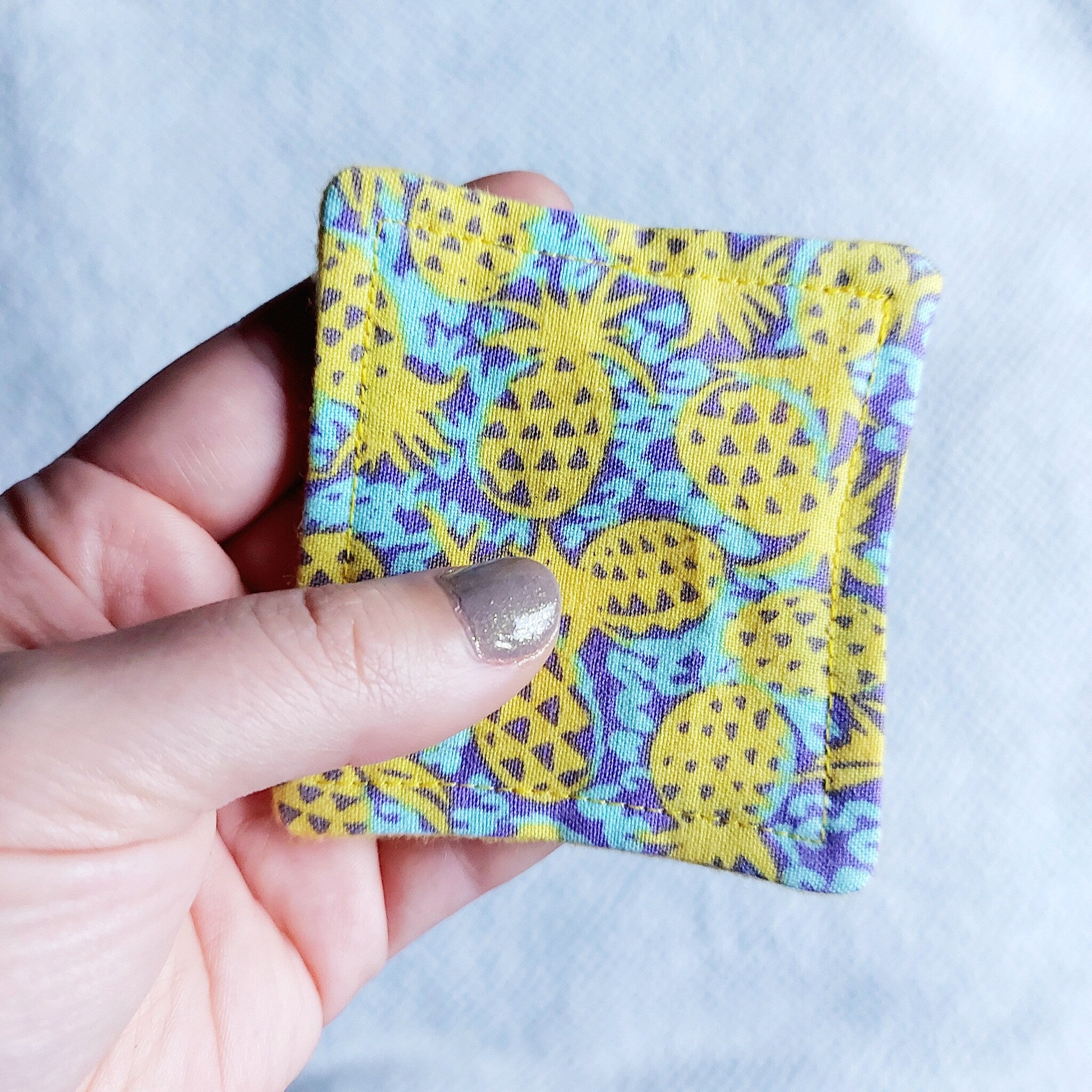Makeup remover pad with yellow pineapple print fabric held in hand