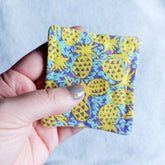 Makeup remover pad with yellow pineapple print fabric held in hand