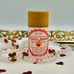 Lip balm tube with paper top and pink striped label, "Cupid's Arrow" text, surrounded by beads