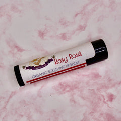 Lip balm tube with white label, black cap, and "Rosy Rosé" text on pink marble background