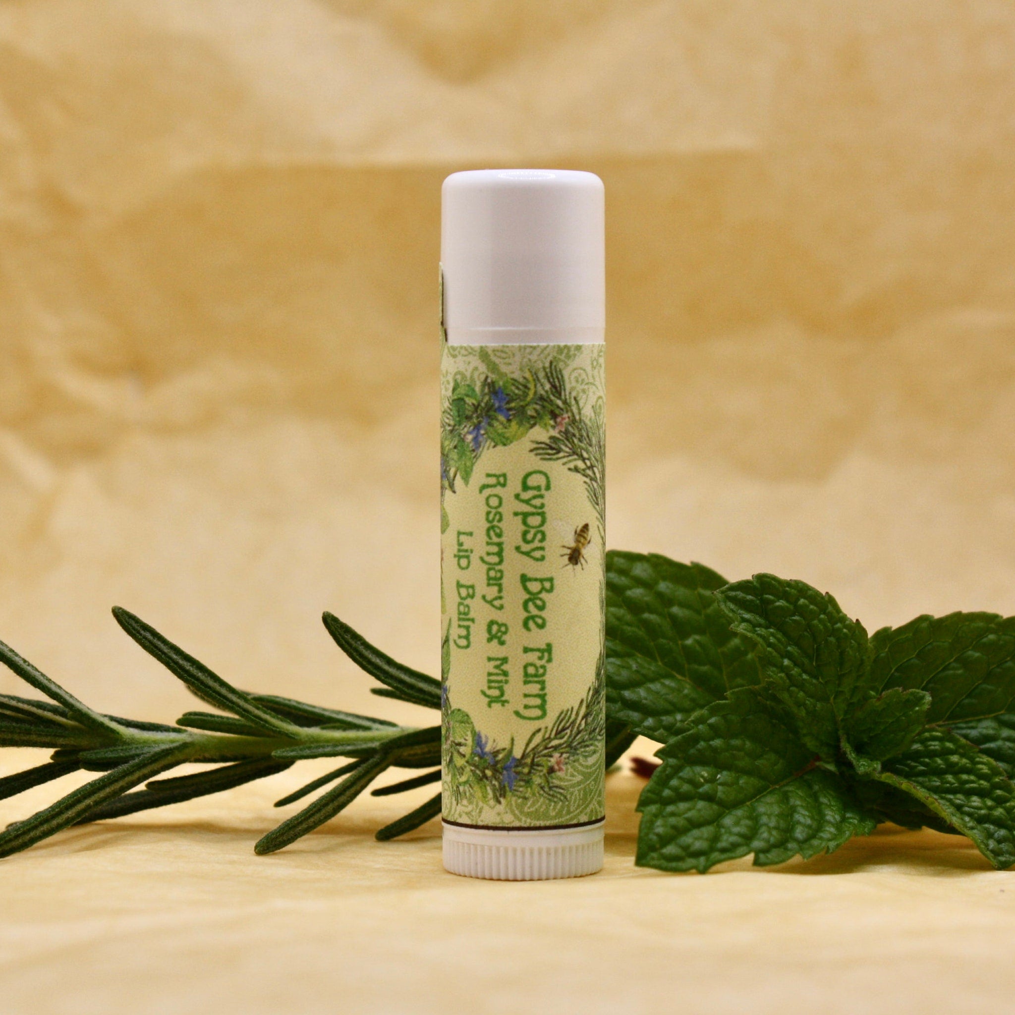 Lip Balm tube with white cap and label, Gypsy Bee Farm branding, and green leaves beside it