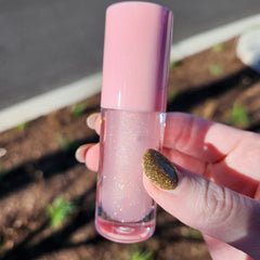 Lip gloss with pink cap, clear tube, and glitter particles, held in hand