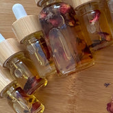 Jojoba oil bottles with rose petals, clear glass, wooden lids, and amber liquid