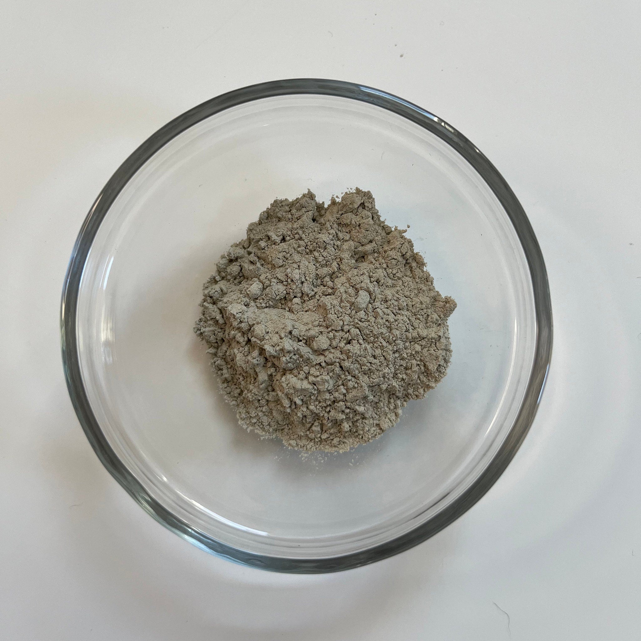 Bentonite clay gray powder in a clear glass bowl on white surface