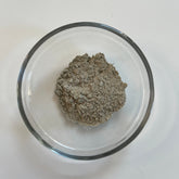 Bentonite clay gray powder in a clear glass bowl on white surface