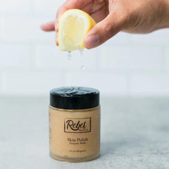 Skin polish jar with black lid, tan color, and Rebel Skincare label with lemon juice dripping over it
