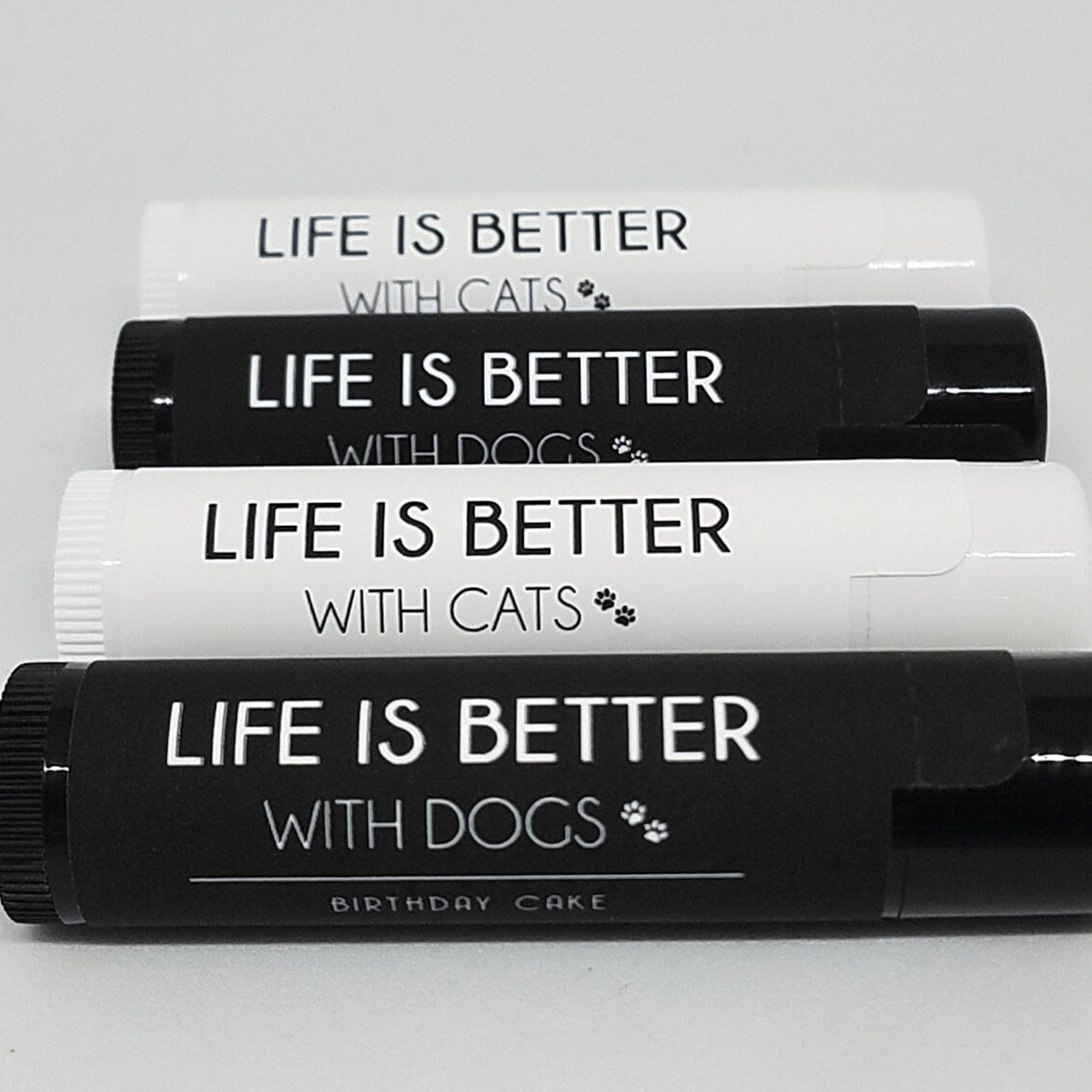 Pet lip balms with black and white labels, text "LIFE IS BETTER" with cats or dogs