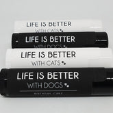 Pet lip balms with black and white labels, text "LIFE IS BETTER" with cats or dogs