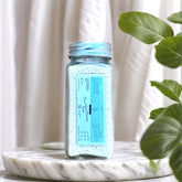 Powder Face Cleanser, clear glass jar with light blue powder, Nizzynaturals label visible on jar, on marble base