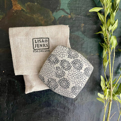 Floral patterned metal object with linen bag, Lisa Jenks for Origins brand visible