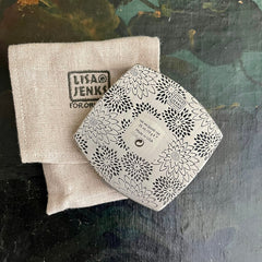 Floral patterned compact with black and white design next to a tan linen pouch, Lisa Jenks brand visible