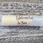 Lip balm tube with "Watermelon Lip Balm" text, clear plastic, and watermelon graphic on wood background
