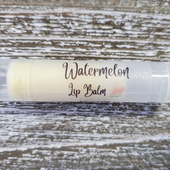 Lip balm tube with "Watermelon Lip Balm" text, clear plastic, and watermelon graphic on wood background
